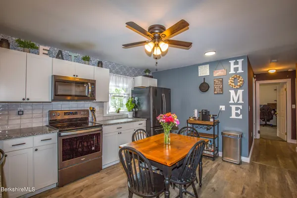 a kitchen with stainless steel appliances kitchen island granite countertop a refrigerator a stove top oven a sink dishwasher and a dining table with wooden floor
