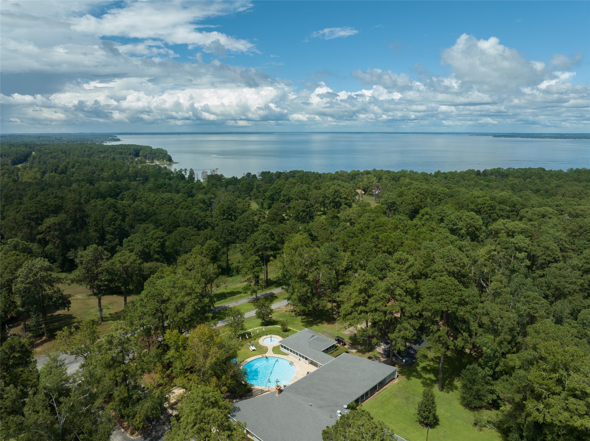 220 North Fairway Loop Coldspring, TX 77331 - Photo 21 of 23 This aerial view showcases the community pool, nestled within a beautifully landscaped area. Surrounded by lush greenery, it offers a peaceful and inviting space to relax, swim, and enjoy sunny days in a tranquil setting. Perfect for both socializing and unwinding, this pool is a true highlight of the community.
