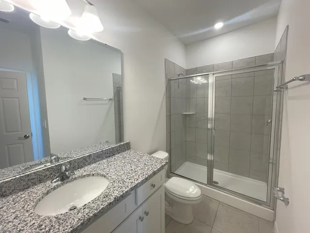 a bathroom with a granite countertop sink a toilet a mirror and shower