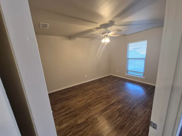 an empty room with wooden floor fan and windows