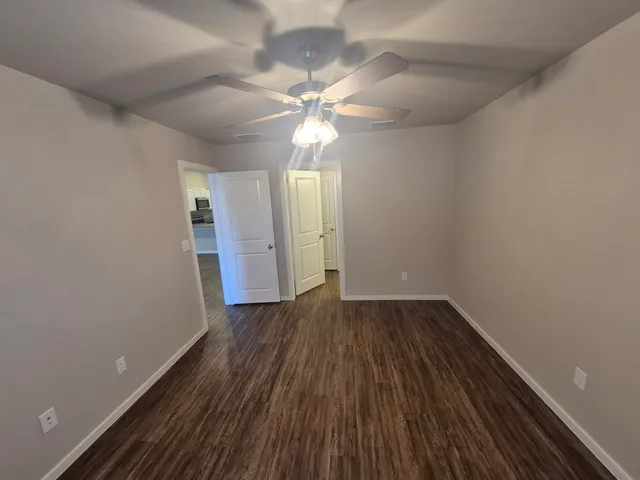 a view of an empty room with wooden floor and a ceiling fan