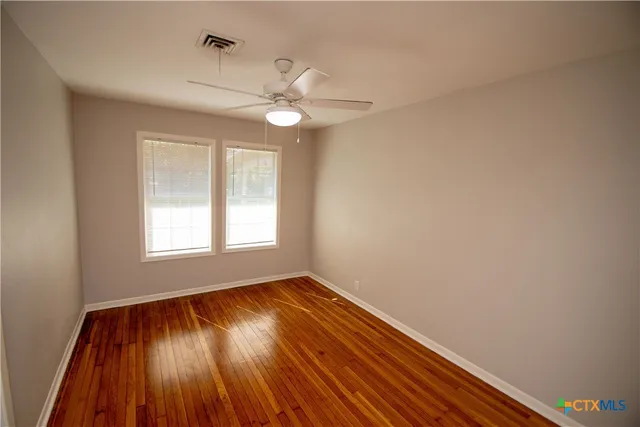 an empty room with wooden floor fan and windows