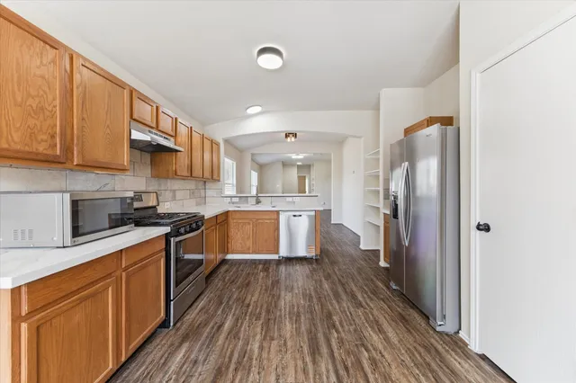 a large kitchen with stainless steel appliances granite countertop a refrigerator a sink dishwasher a stove and white countertops with wooden floor