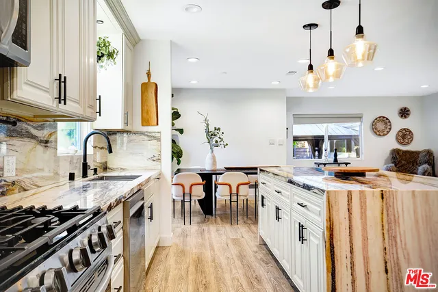 a kitchen with stainless steel appliances granite countertop a stove a sink dishwasher and a dining table with wooden floor