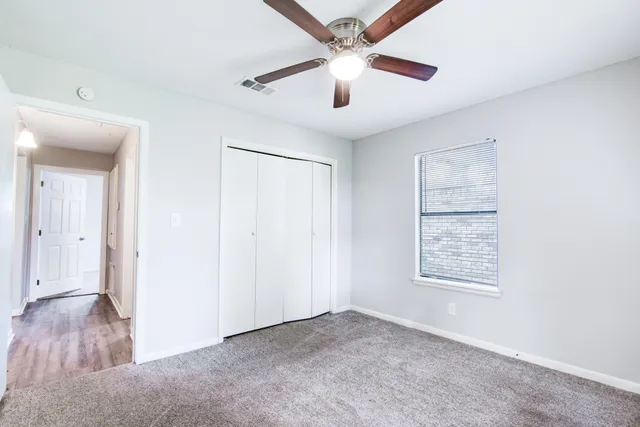 an empty room with wooden floor ceiling fan and windows