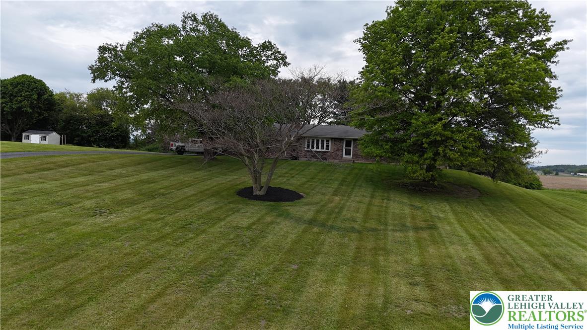 8813 Bluejay Road Kempton, PA 19529 - Photo 22 of 23 This expansive green lawn frames a charming brick house and a separate storage shed, all beneath a vast sky.