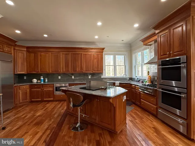 a kitchen with granite countertop wooden floors stainless steel appliances a sink and cabinets