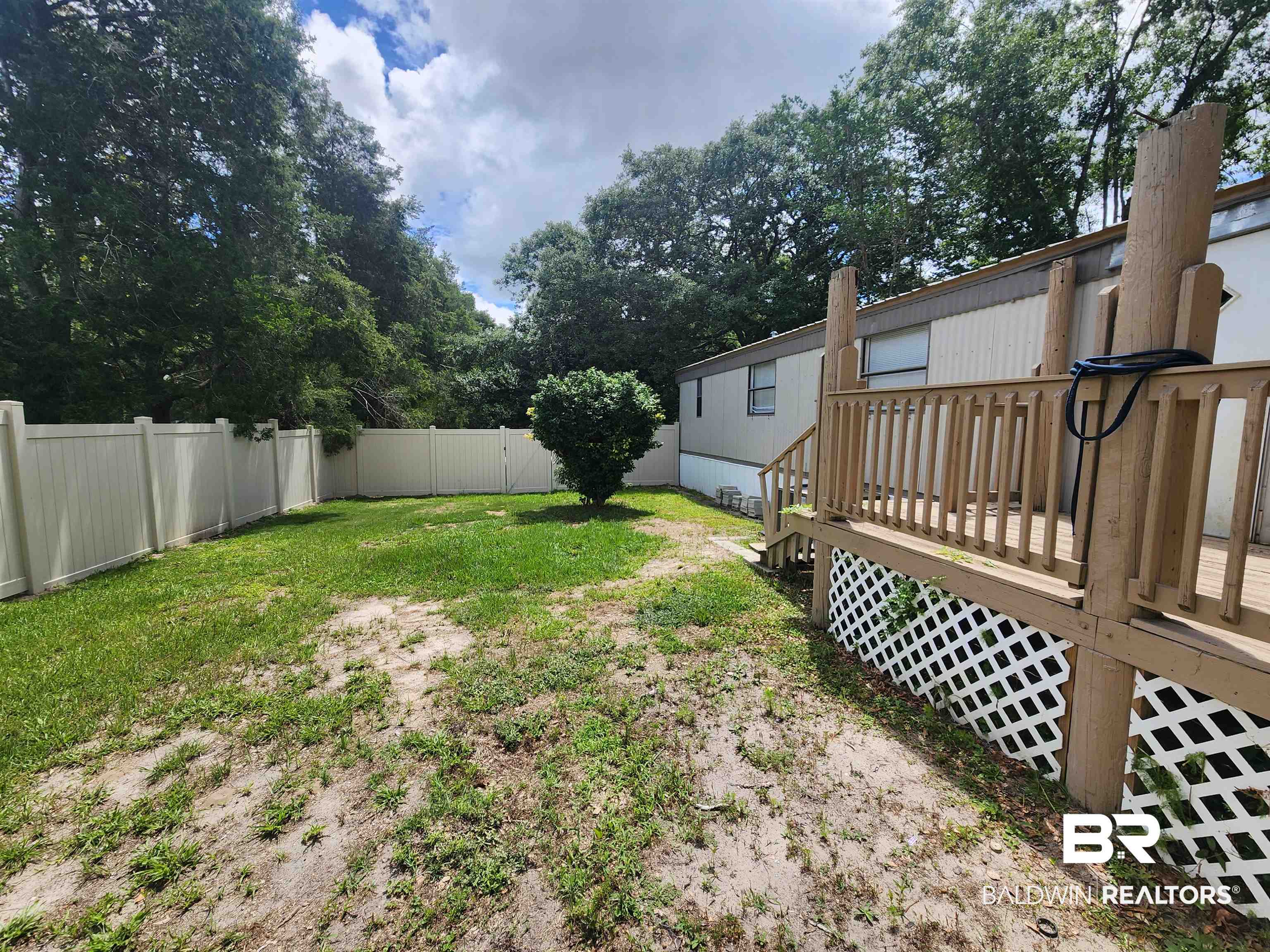 23051 Fritz Lane Foley, AL 36535 - Photo 6 of 26 Fenced backyard featuring a wood deck with lattice skirting, mature trees, and a central shrub