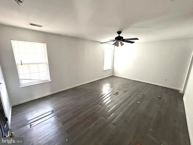 an empty room with wooden floor ceiling fan and windows