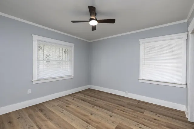 an empty room with wooden floor ceiling fan and windows
