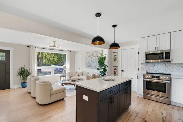 a open kitchen with stainless steel appliances granite countertop a stove a sink dishwasher and a fireplace with wooden floor