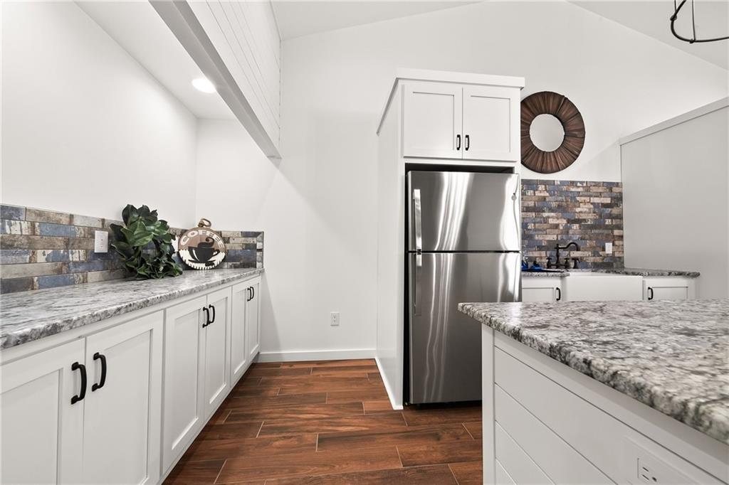 611 Padgetts Road Opelika, AL 36804 - Photo 52 of 64 White shaker-style cabinetry with black hardware, stainless steel refrigerator, stone-look countertops, brick-patterned backsplash, and wood-finish flooring