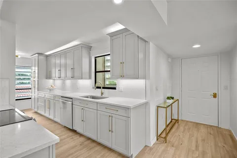 a kitchen with a sink dishwasher a stove and white cabinets with wooden floor