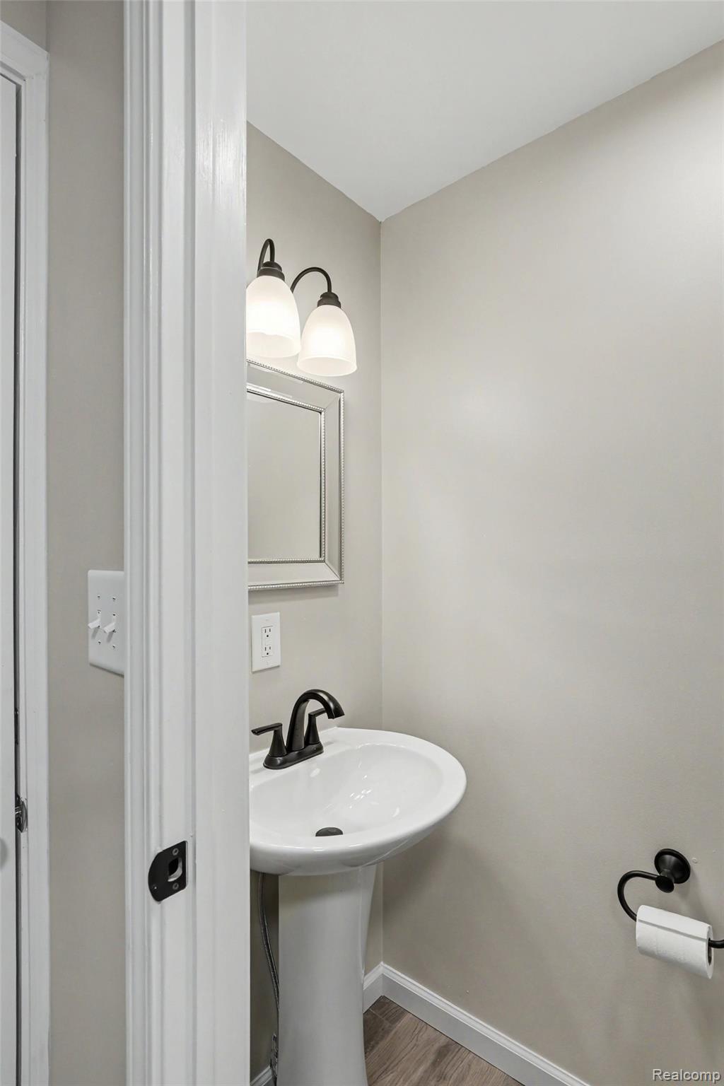74600 Nordman Court Romeo, MI 48065 - Photo 18 of 32 Pedestal sink with matte black faucet, wall-mounted light fixture, framed mirror, and wood-finish flooring