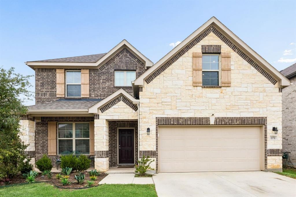 Two-story residence featuring a brick and stone exterior, a two-car garage, and established landscaping