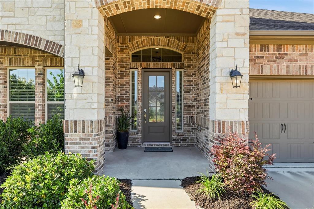 4017 Eagles Bluff Road Midlothian, TX 76065 - Photo 5 of 38 Brick and stone facade featuring a covered entry, arched brick detailing, a glass panel front door, and exterior sconce lighting