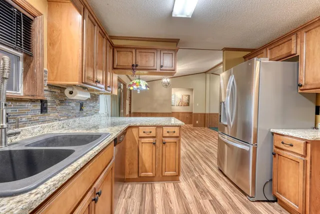 a kitchen with stainless steel appliances granite countertop a refrigerator a sink and dishwasher with wooden floor