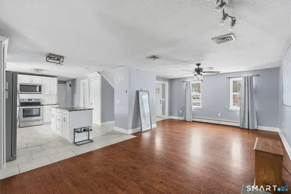 a view of an empty room with wooden floor and a kitchen