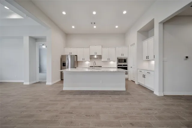 a view of kitchen with kitchen island white cabinets stainless steel appliances with a sink and cabinets