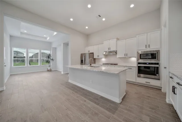 a large kitchen with stainless steel appliances granite countertop a stove a sink a refrigerator and white cabinets with wooden floor