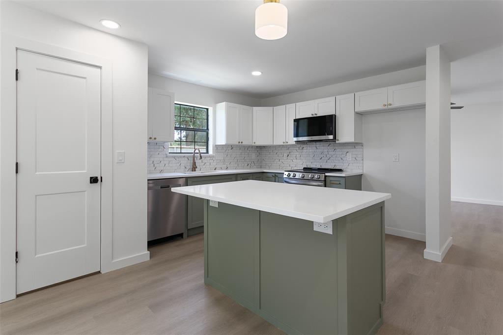 1346 South Reno Road Springtown, TX 76082 - Photo 2 of 24 Modern kitchen featuring a central island with a white countertop, two-tone cabinetry with green base and white upper cabinets, stainless steel appliances, and wood-finish flooring