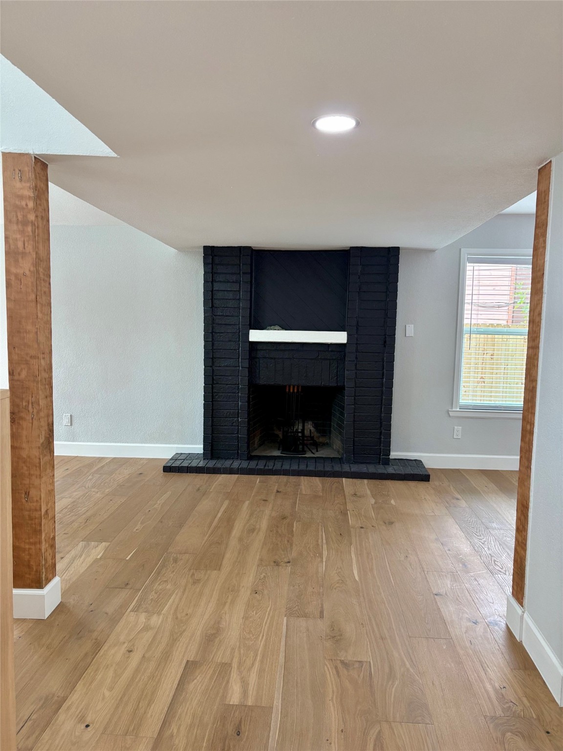 12303 Split Rail Lane Houston, TX 77071 - Photo 22 of 50 Captured from afar, the view highlights the elegant flow of the living space, showcasing warm engineered white oak floors and beautiful cedar posts that frame the brick fireplace as the room’s focal point.