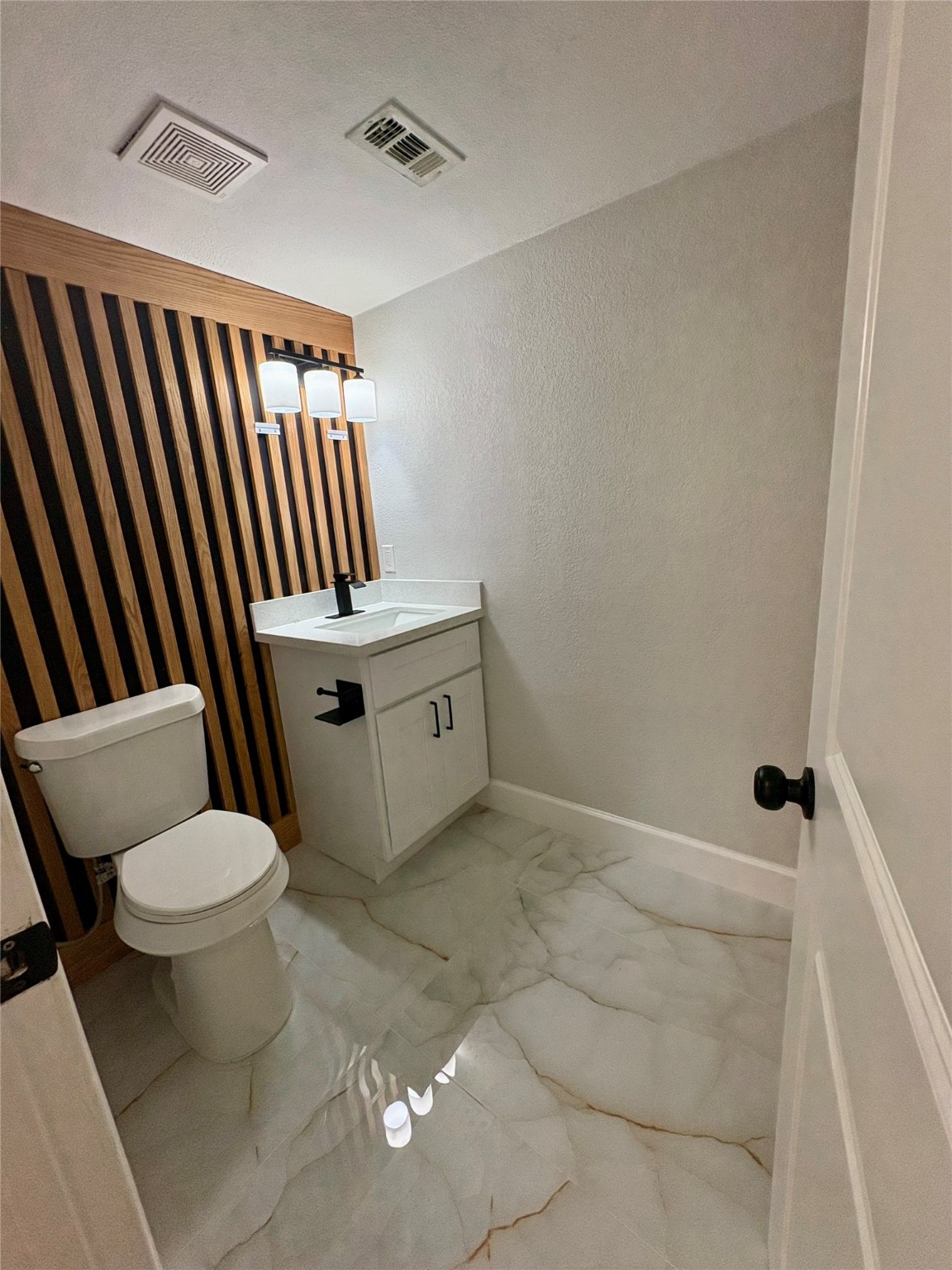 12303 Split Rail Lane Houston, TX 77071 - Photo 25 of 50 The stylish half bath features a striking wood accent panel, a brand-new toilet, modern vanity with a quartz countertop, contemporary light fixture, and elegant modern tile flooring that together create a clean, sophisticated look.