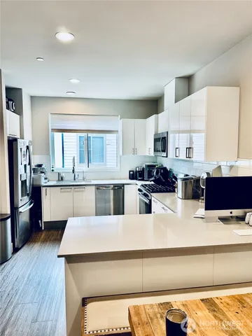 a living room with stainless steel appliances kitchen island granite countertop a refrigerator a stove a sink dishwasher and white cabinets with wooden floor