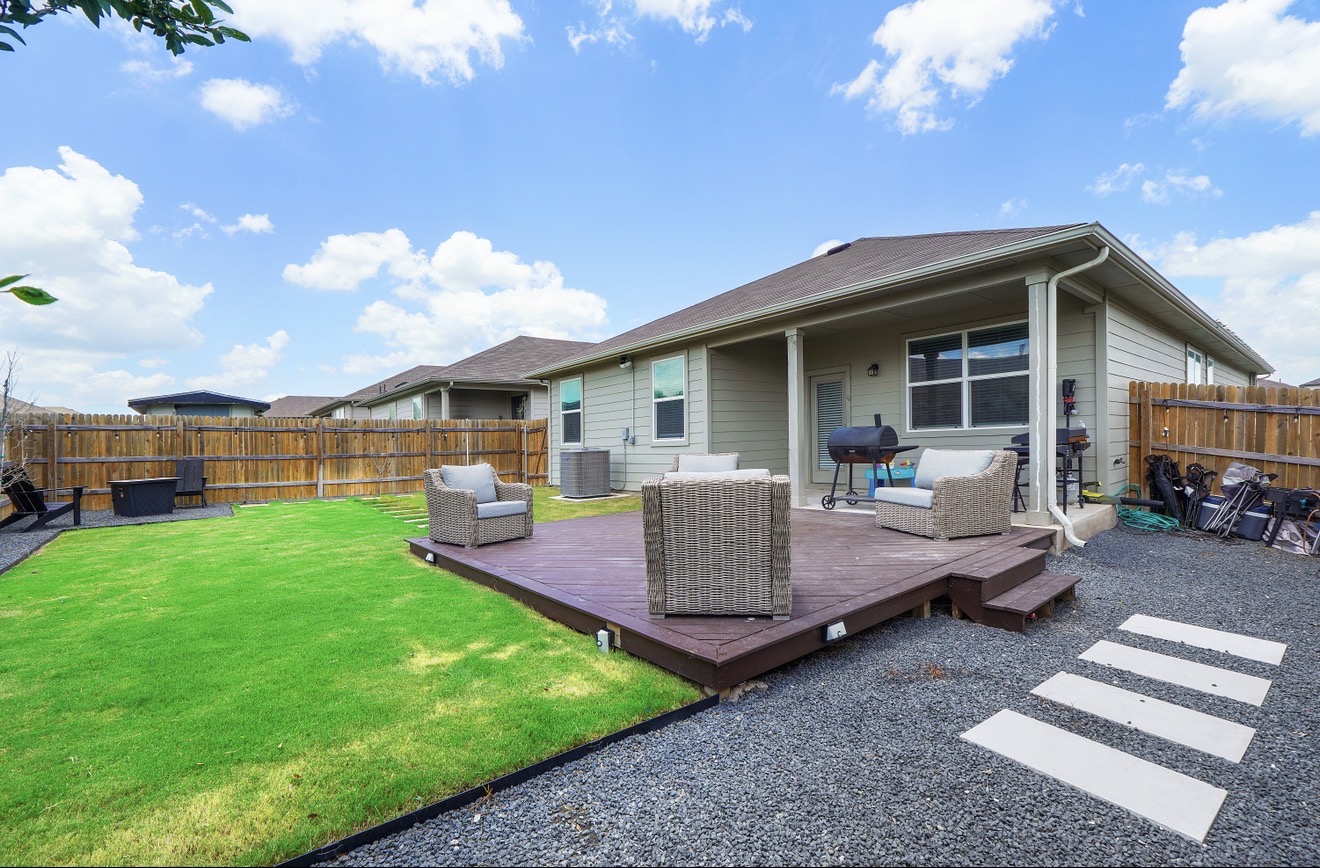 217 Evergreen Sumac Loop Kyle, TX 78640 - Photo 3 of 20 A fenced backyard offers a wooden deck and vibrant green lawn, perfect for outdoor enjoyment.