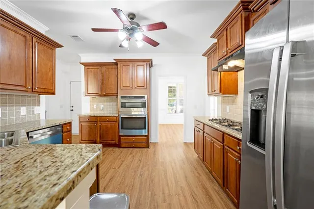 a kitchen with stainless steel appliances granite countertop a refrigerator a stove top oven a sink dishwasher and wooden cabinets with wooden floor