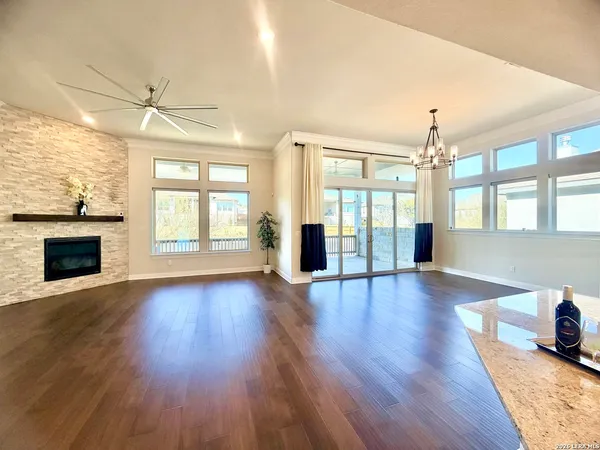 an empty room with wooden floor chandelier fan and windows