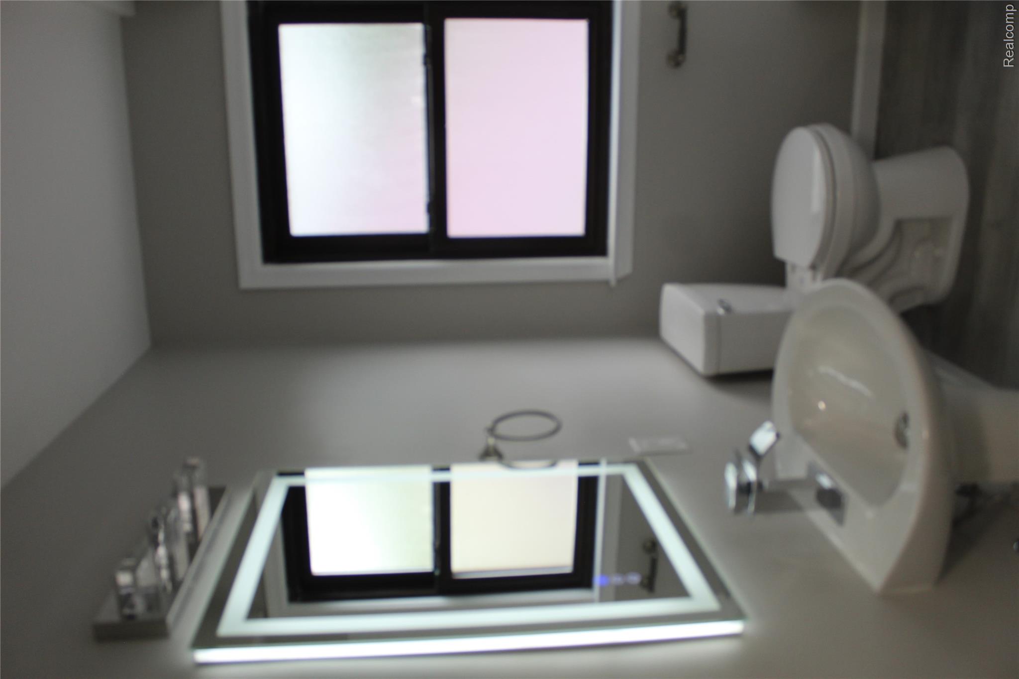 5543 Balfour Road Detroit, MI 48224 - Photo 38 of 54 Bathroom featuring a pedestal sink, framed mirror with integrated lighting, window with white trim and dark frame, and wood-finish flooring