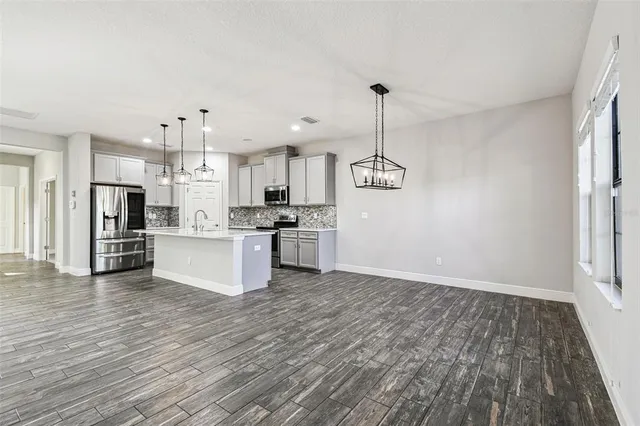 a open kitchen with stainless steel appliances a refrigerator a sink dishwasher a stove and white cabinets with wooden floor