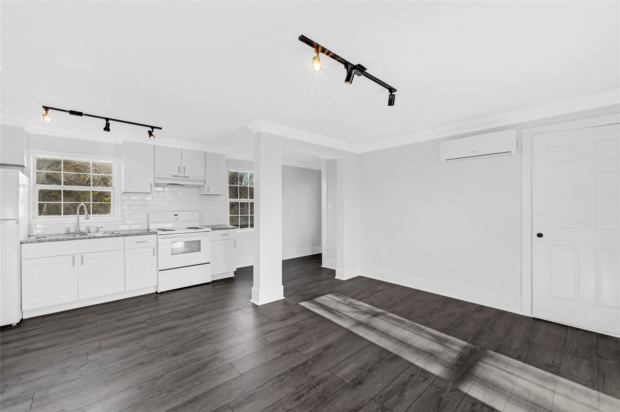 1633 Fourcade Street, Unit C Houston, TX 77023 - Photo 3 of 7 Bright, modern kitchen with white cabinetry, subway tile backsplash, and dark wood flooring. Features track lighting, large windows, and an open layout for easy living and entertaining.