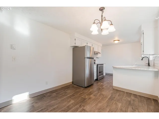 a kitchen with stainless steel appliances granite countertop a refrigerator a sink dishwasher and a dining table with wooden floor