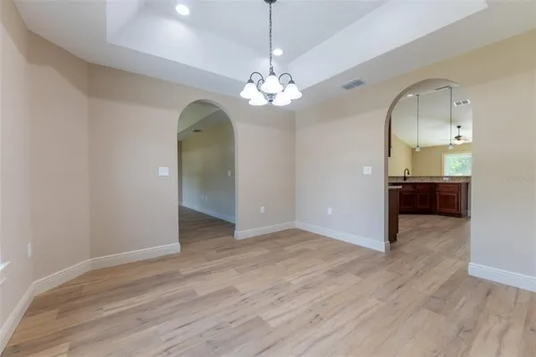 an empty room with wooden floor chandelier and windows