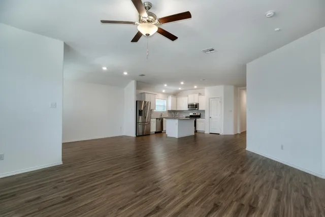 a view of an empty room with wooden floor and a ceiling fan