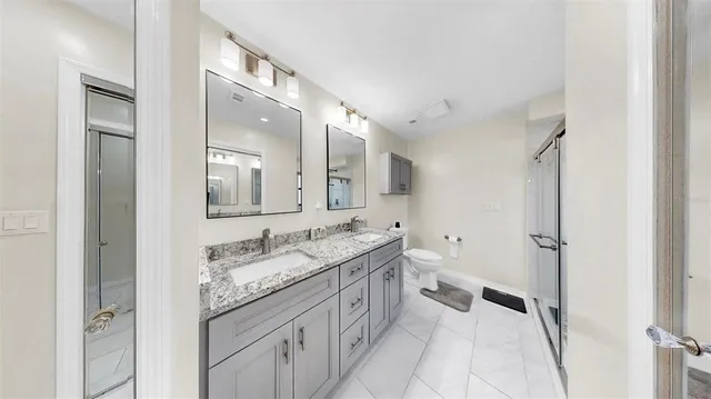 a spacious bathroom with a granite countertop double vanity sink a mirror and a shower