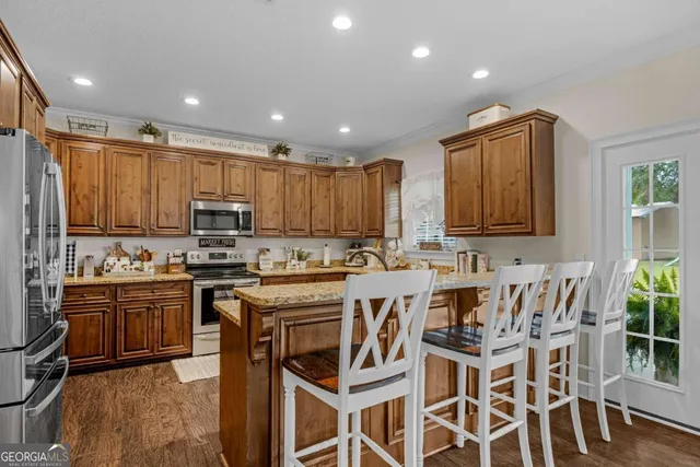 a kitchen with stainless steel appliances granite countertop a stove top oven a sink dishwasher and a refrigerator with wooden floor