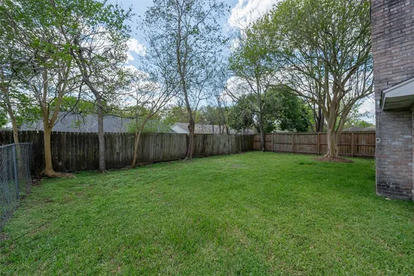 a view of a backyard with large trees and wooden fence