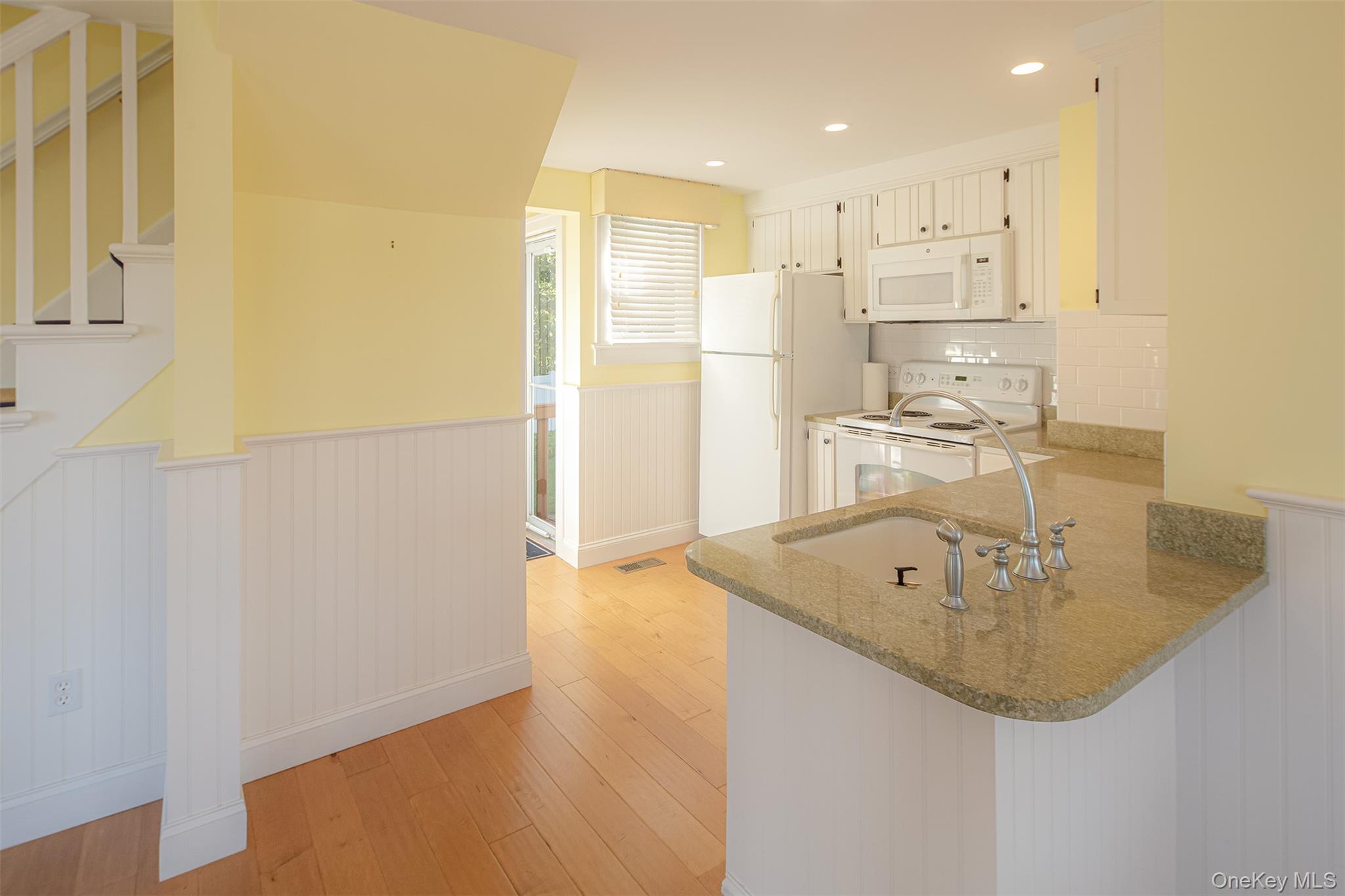 1 Canal Road Hampton Bays, NY 11946 - Photo 11 of 50 Kitchen with wainscoting, white appliances, light wood-style flooring, light stone counters, and tasteful backsplash