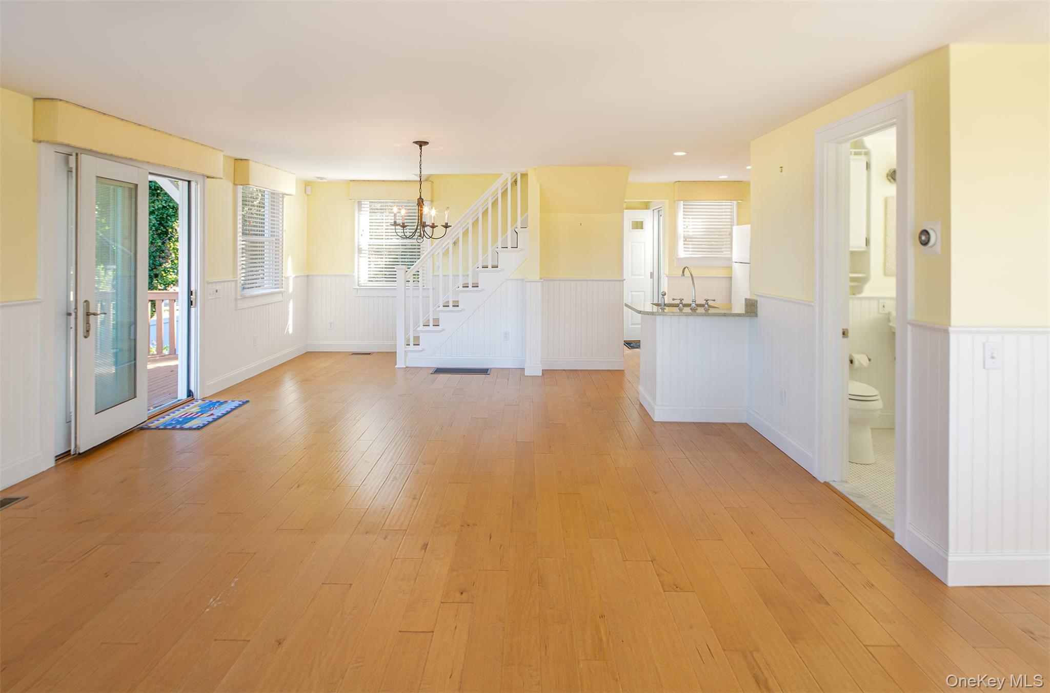 1 Canal Road Hampton Bays, NY 11946 - Photo 16 of 50 Unfurnished dining area featuring a wainscoted wall, light wood-style flooring, a chandelier, and stairway