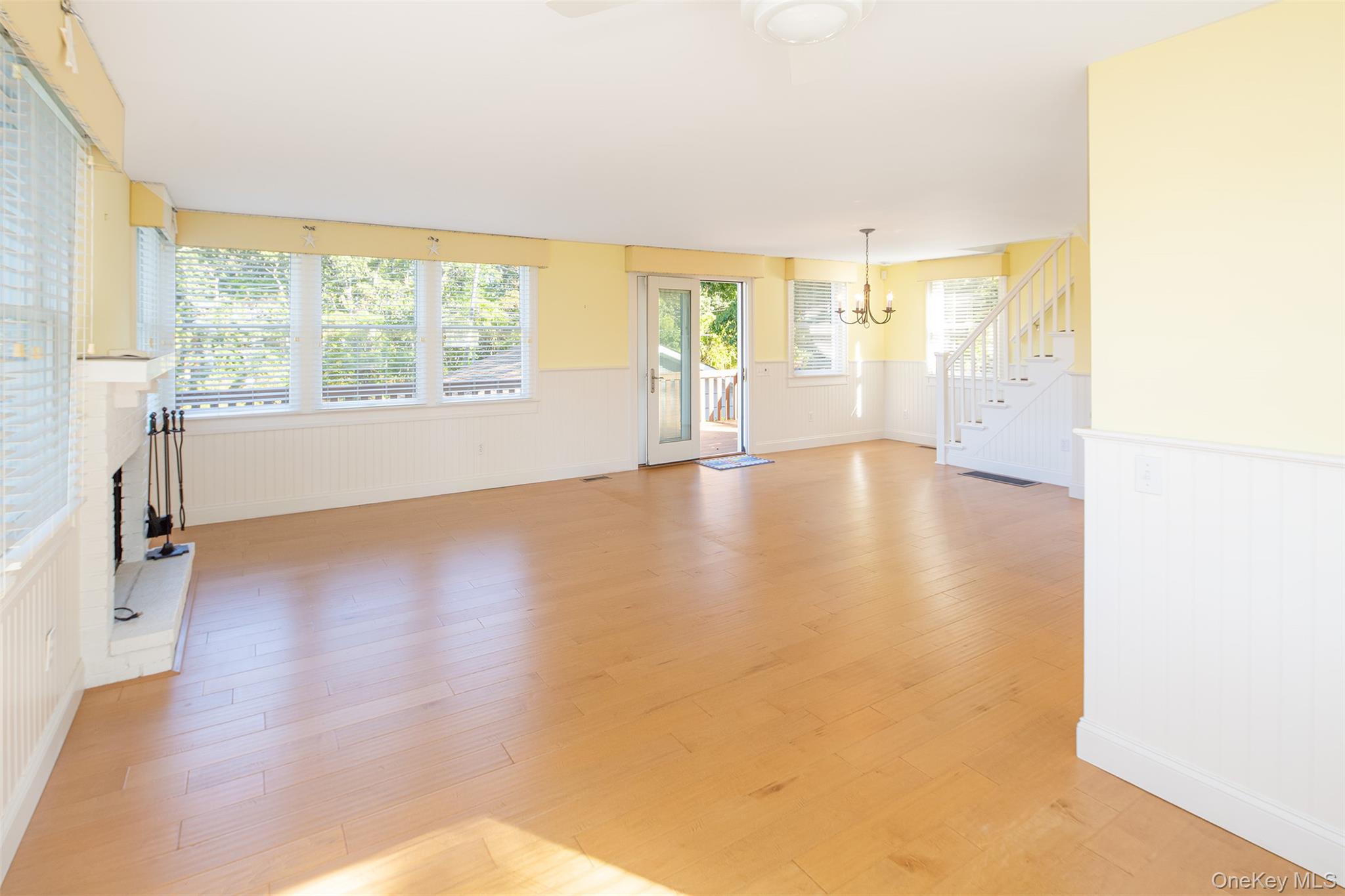 1 Canal Road Hampton Bays, NY 11946 - Photo 17 of 50 Unfurnished living room with a wainscoted wall, stairway, a brick fireplace, light wood-type flooring, and a chandelier