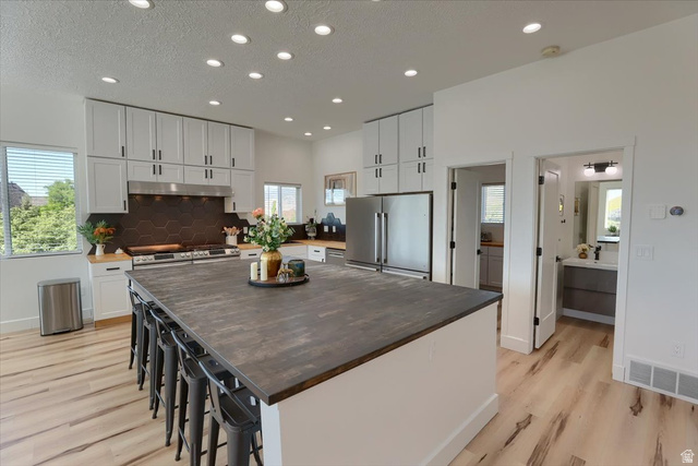 828 South Deer Road Tooele, UT 84074 - Photo 11 of 51 Open-concept kitchen featuring light-finish flooring, recessed lighting, white cabinetry with dark hardware, a center island with seating, and stainless steel appliances