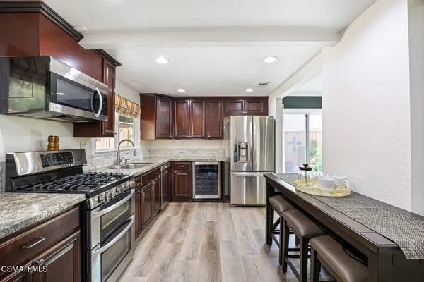 a kitchen with stainless steel appliances granite countertop a stove top oven a sink dishwasher a refrigerator and a dining table with wooden floor
