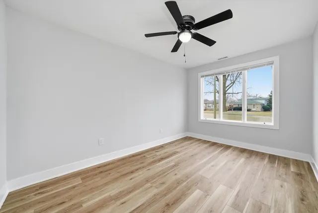 an empty room with wooden floor fan and windows