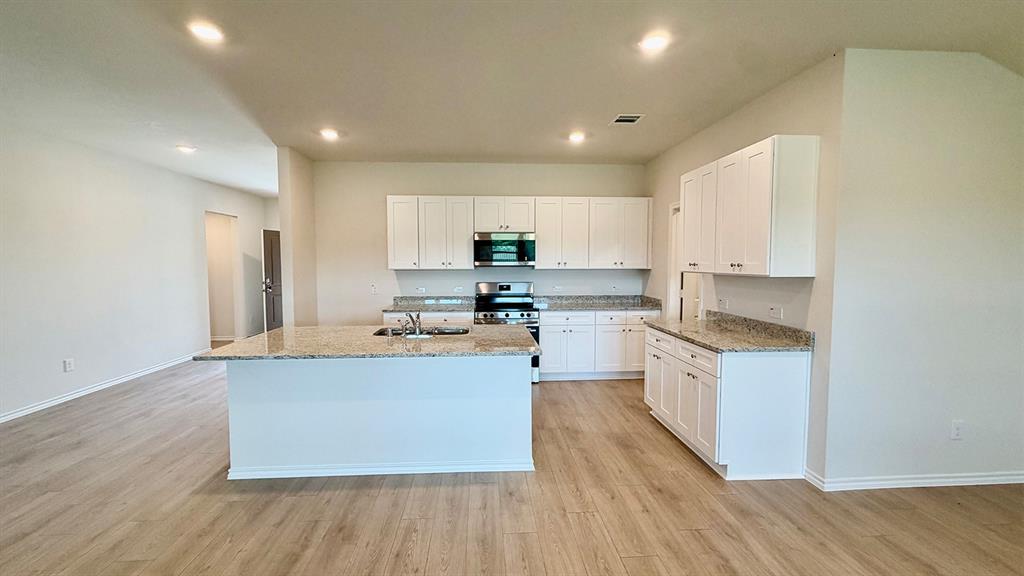 2003 Reveille Way Terrell, TX 75160 - Photo 12 of 25 Open-concept kitchen with a central island, recessed lighting, wood-finish flooring, white cabinetry, and light-toned countertops