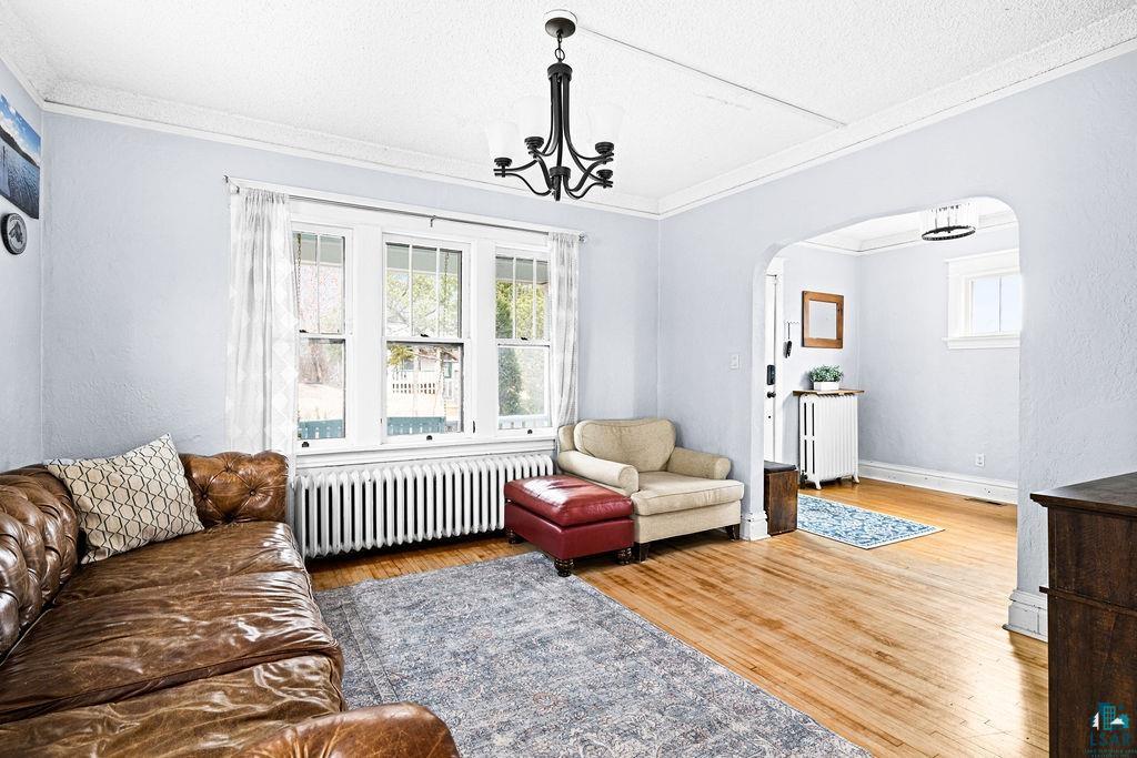 4608 Regent Street Duluth, MN 55804 - Photo 13 of 43 Living area with radiator, wood finished floors, arched walkways, crown molding, and a notable chandelier