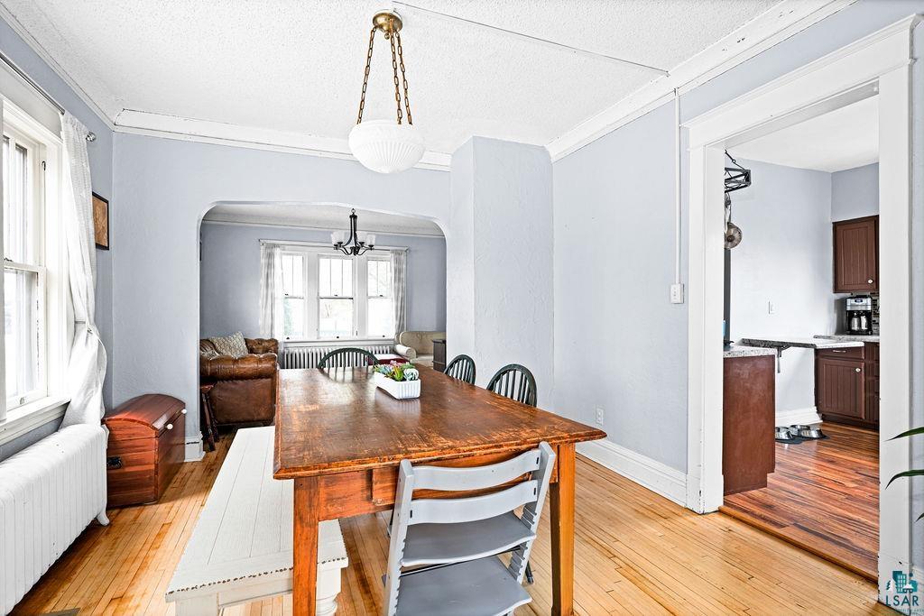 4608 Regent Street Duluth, MN 55804 - Photo 15 of 43 Dining space featuring radiator heating unit, arched walkways, ornamental molding, light wood-style floors, and a chandelier