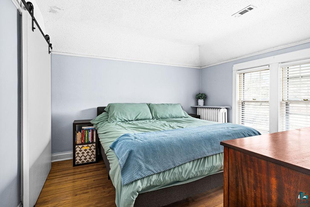4608 Regent Street Duluth, MN 55804 - Photo 22 of 43 Bedroom featuring visible vents, a textured ceiling, wood finished floors, a barn door, and lofted ceiling